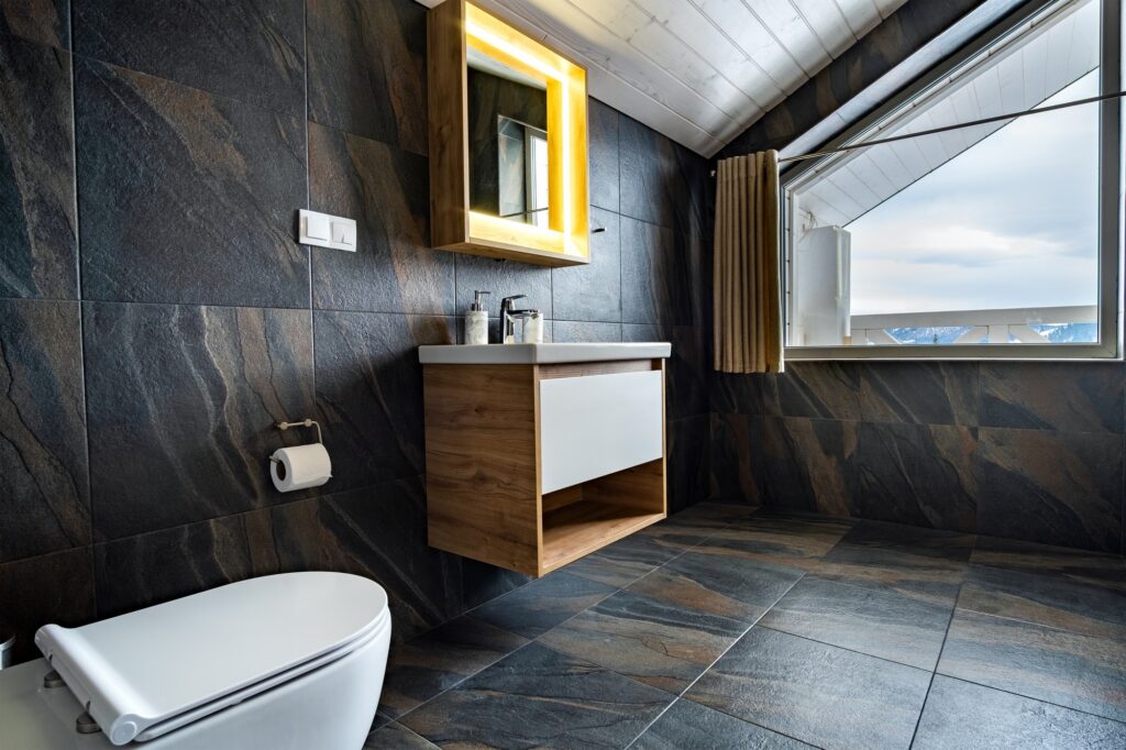 Interior of modern stylish bathroom with black tiled walls, curtain shower place and wooden